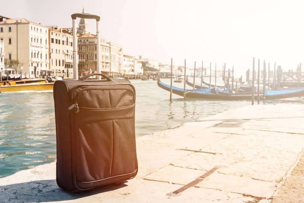 Brown leather suitcase on Venice waterfront with gondolas and historic buildings